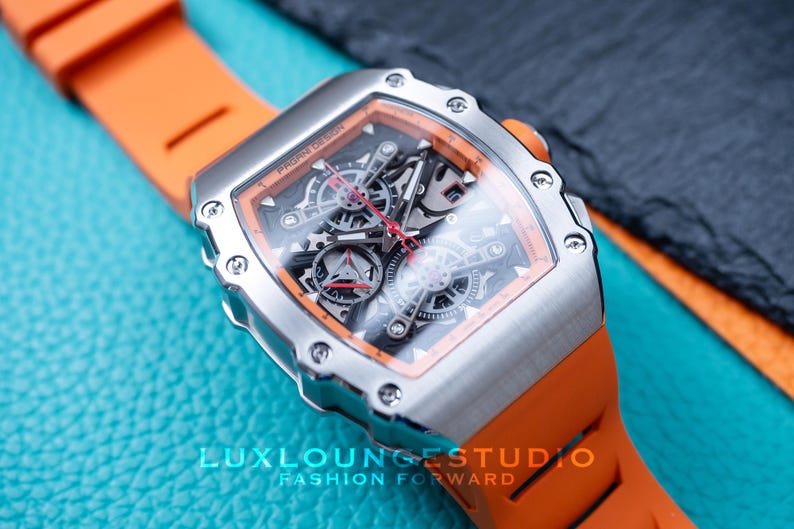 Peut inclure: Une montre-bracelet argent&eacute;e avec un bracelet orange. Le cadran de la montre est transparent, r&eacute;v&eacute;lant les m&eacute;canismes internes. La montre est pos&eacute;e sur un fond bleu et noir. Le texte "PAGANI DESIGN" est visible sur le cadran.
