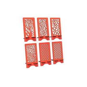 May include: A set of six bright orange phone stands, each featuring a unique laser-cut pattern including tree branches, leaves, geometric shapes, and grid designs. These upright rectangular holders have a small shelf for device support.