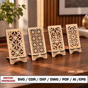 May include: Four light-coloured wooden phone stands with intricate laser-cut patterns. Each stand features a rectangular back panel with unique floral or scrollwork cutouts and a small shelf for a device. Text on the image reads 3MM - 4MM.