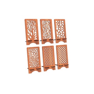 May include: A set of six rectangular brown wooden phone stands, each featuring a unique laser-cut pattern including tree branches, leaves, geometric shapes, and floral motifs. Each stand has a base support ledge and a curved cutout at the bottom.