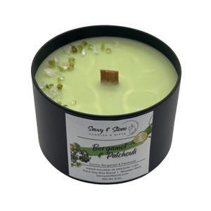 May include: A black candle jar with a green wax candle and a wooden wick. The candle is topped with green and white crystals. The label reads "Savvy & Stone Candles & Gifts Bergamot & Patchouli Scents: Bergamot & Patchouli HAND POURED IN OREGON USA Para-Soy Wax Blend | Wooden Wick Savvyandstone.com Net Wt. 6 oz."