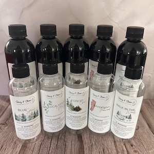 May include: Ten clear glass bottles with black lids filled with scented reed diffuser oil. The bottles are labeled with different scents, including Blue Spruce, Eucalyptus & Mint, Forest Chai, Mahogany & Sandalwood, and Walk in the Woods.