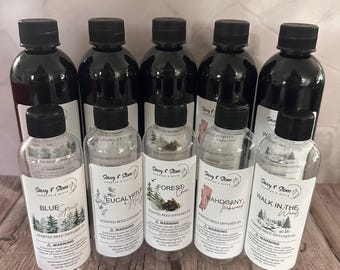 May include: Ten clear glass bottles with black lids filled with scented reed diffuser oil. The bottles are labeled with different scents, including Blue Spruce, Eucalyptus & Mint, Forest Chai, Mahogany & Sandalwood, and Walk in the Woods.