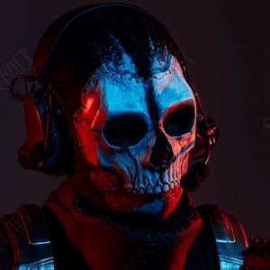 May include: A person in a tactical outfit, wearing a skull mask with headphones, and holding a rifle. The mask is white with black details, and the scene is lit with red and blue lights. The text "Dominus.Cosplay" is visible.