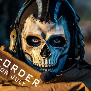 Puede incluir: Una máscara táctica con diseño de calavera blanca, cuencas oculares y cavidad nasal negras, usada con auriculares de comunicación color canela y un micrófono. El texto PRE-ORDER FOR JULY está superpuesto en diagonal en blanco.