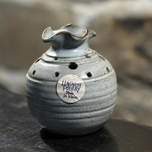 May include: A white ceramic pot with a scalloped rim and holes in the sides. The pot has a label that reads "Llanarth Pottery Made in Wales".