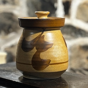 Puede incluir: Un tarro de cerámica con tapa, decorado con diseños abstractos marrones sobre un fondo beige.