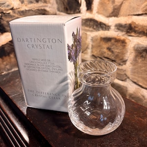 May include: A clear glass Dartington Crystal ripple vase or candleholder with a rounded body and a flared, twisted rim. It is accompanied by its original white cardboard box featuring the text Dartington Crystal, Ripple Vase or Candleholder FT266.