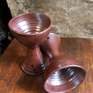 May include: Two brown ceramic cups with a flared base and a wide, rounded top. The cups are made of a textured clay and have a rustic, handmade look.