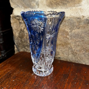 May include: A clear glass vase with a blue base and intricate cut glass design. The vase has a wide mouth and a narrow base.