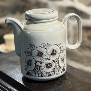 May include: A white ceramic teapot with a brown floral design. The teapot has a lid and a handle.