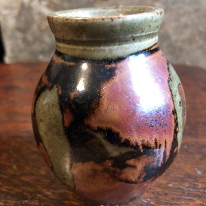 May include: A small, round ceramic vase with a brown, green and pink glaze. The vase has a wide mouth and a narrow base.