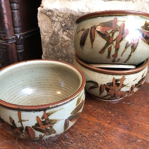 May include: Three ceramic bowls with a brown and white speckled glaze and a brown floral design. The bowls are stacked on top of each other.
