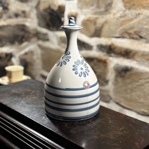 May include: A white ceramic pitcher with blue and white floral designs and blue stripes. The pitcher has a narrow neck and a wide base.