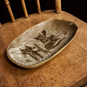 May include: A brown and white ceramic dish with a design of three stylized cats in brown glaze.