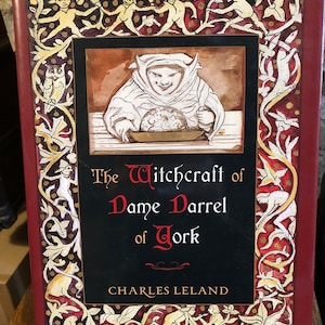 May include: A red book cover with a black and gold illustration of a person in a hooded robe holding a bowl. The title of the book is "The Witchcraft of Dame Darrel of York" by Charles Leland.