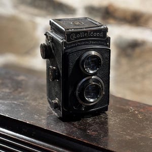 May include: A black Rolleicord camera with two lenses and a silver nameplate that reads "Rolleicord Franke & Heidecke Braunschweig".