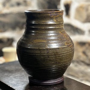 May include: A dark brown ceramic vase with a textured, ribbed surface. The vase has a rounded body and a slightly flared lip.