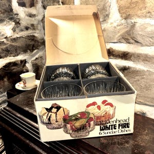May include: A box of six clear glass sundae dishes with a white fire design. The box is open and the dishes are visible inside. The box is labeled "Ravenhead White Fire 6 Sundae Dishes".