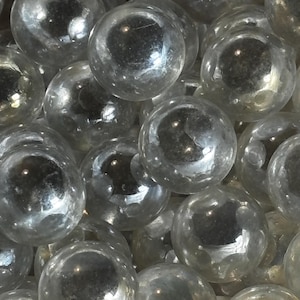 Puede incluir: Primer plano de una colección de canicas de vidrio transparente. Las canicas esféricas reflejan la luz, creando reflejos y sombras. Las canicas son un juguete y un artículo decorativo popular.