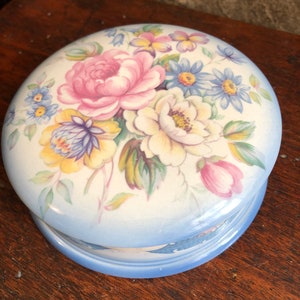 以下が含まれることがあります： 花柄のヴィンテージ磁器製の小物入れ。蓋は青と白の花柄で、ピンク、黄色、白の花が描かれています。箱の底は薄い青色です。