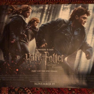 May include: A movie poster for the film "Harry Potter and the Deathly Hallows: Part 1." The poster features Harry Potter, Hermione Granger, and Ron Weasley in a forest setting. The text on the poster reads "Nowhere is safe" and "Harry Potter and the Deathly Hallows: Part 1." The poster also includes the release date "November 19."
