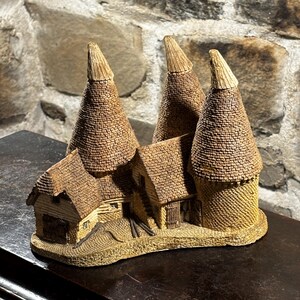 Könnte beinhalten: Eine detaillierte Miniaturskulptur einer rustikalen Dorflandschaft. Die Skulptur zeigt mehrere kegelförmige Strukturen mit strukturierten, braunen Außenflächen, die an Öfen oder Türme erinnern, sowie kleine Gebäude mit Satteldächern. Der Sockel ist hellbeige.