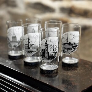 May include: Set of six clear glass tumblers with black and white illustrations of cityscapes. Each tumbler features a different cityscape design.