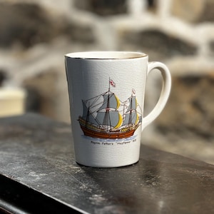 May include: White ceramic mug with a gold rim. The mug features a colorful illustration of the Mayflower ship with the text "Pilgrim Fathers - Mayflower - 1620".