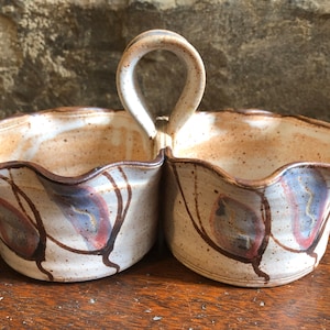 May include: A white ceramic serving dish with a brown handle and a brown, blue, and pink leaf design. The dish is divided into two sections.