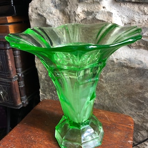 May include: A green glass vase with a wide, flared opening and a geometric base. The vase has a textured, faceted design.