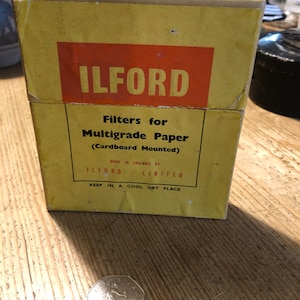 Może przedstawiać: Żółte pudełko z tekstem "ILFORD Filtry do papieru wielogradacyjnego (zamontowane na kartonie)" i "WYPRODUKOWANO W ANGLII PRZEZ ILFORD LIMITED PRZECHOWYWAĆ W CHŁODNYM I SUCHYM MIEJSCU".