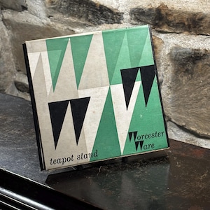 Puede incluir: Un soporte para tetera negro y verde con un patrón geométrico y el texto "Worcester Ware" y "teapot stand".