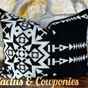 May include: Black and white geometric patterned throw pillow with a black background and white geometric designs. The pillow is on a wooden surface with the text "Cactus & Cowponies" in gold lettering.