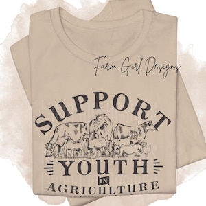 May include: Beige t-shirt with the text "SUPPORT YOUTH IN AGRICULTURE" in black. The design includes illustrations of farm animals such as cows, goats, and a horse. The words "Farm Girl Designs" are written in cursive at the top.