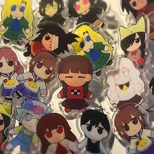 Puede incluir: Una colección de colgantes acrílicos de personajes de estilo anime. Los colgantes presentan varios personajes con peinados, ropa y expresiones distintivas. La paleta de colores incluye tonos de amarillo, verde, rojo y azul.