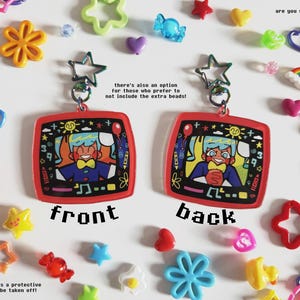 May include: Two red, square-shaped keychains with cartoon illustrations, labeled "front" and "back", are displayed. The keychains are surrounded by colorful plastic charms, including stars, flowers, and hearts. The text "are you still watching?" is visible.