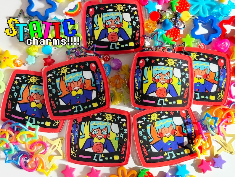 May include: Red-framed charms featuring a cartoon character with blue hair and a yellow bow tie, set against a black background with musical notes and numbers. The word "STATIC charms!!!!" is displayed in a pixelated font. Assorted colorful charms surround the main objects.