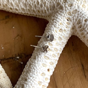 May include: A pair of silver stud earrings, one with a small circle and the other with a small cross.