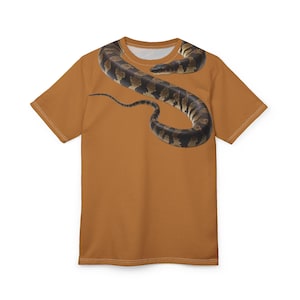 May include: A rust-coloured t-shirt with a detailed illustration of a snake. The snake is brown and black with a patterned design, and it is wrapped around the shirt. The shirt has a crew neck.