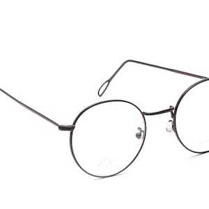 Op de afbeelding: Ronde bril met een dun, donker metalen montuur. De glazen zijn helder en de pootjes hebben een eenvoudig, gebogen ontwerp. De bril heeft een minimalistische uitstraling.
