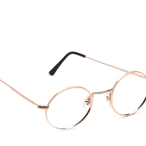 Peut inclure: Lunettes rondes en métal rose gold avec des montures fines et des verres transparents.