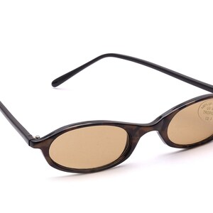 Könnte beinhalten: Ovale Sonnenbrille in Schildpatt-Optik mit braunen Gläsern. Die Sonnenbrille hat ein Etikett auf dem rechten Glas, auf dem "100% UV 400, Tropical, CE" steht.