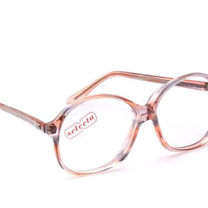 Può includere: Occhiali vintage con montatura trasparente e color pesca. Gli occhiali hanno una forma rotonda e il marchio "selecta" è visibile sulla lente. Le aste sono di colore marrone chiaro con un motivo decorativo. Fatto in Francia.