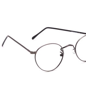 Può includere: Occhiali con montatura rotonda con montatura in metallo grigio scuro. Gli occhiali hanno un design classico e minimalista con aste sottili e un ponte. Le lenti sono trasparenti e l'estetica generale è moderna e sobria.