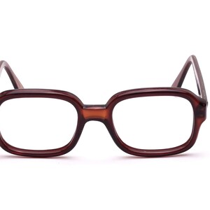 Può includere: Occhiali rettangolari marroni dal design classico. Le montature sono di un colore marrone caldo e uniforme, e le lenti sono trasparenti. Gli occhiali hanno un'estetica vintage, adatta all'uso quotidiano.