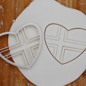 May include: A white plastic heart-shaped cookie cutter with a cross-hatch design. The cutter is shown on a white fondant surface.
