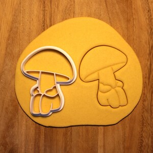 May include: Two white plastic cookie cutters shaped like mushrooms. The cutters are on a yellow surface.