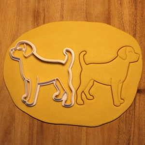 May include: Two dog-shaped cookie cutters on a yellow surface. The cutters are made of white plastic and are ready to be used to make cookies.