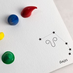 May include: A white card with a black outline of the constellation Aries, labeled "Aries". Four paint colors are shown: red, blue, yellow, and green.